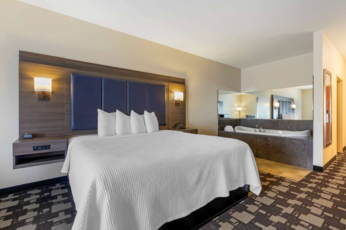 A hotel room with a large bed, a built-in desk, a vanity with a mirror, and a bathtub.