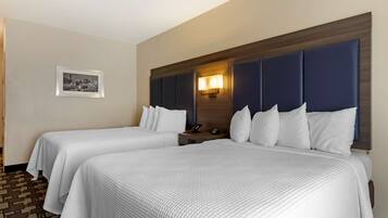 A hotel room with two beds, a nightstand, a wall-mounted lamp, and a framed picture on the wall.