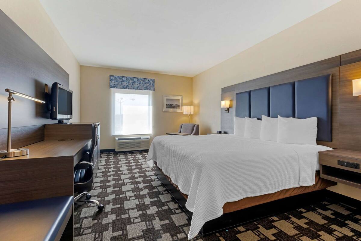 A hotel room with a bed, desk, chair, TV, and a window.