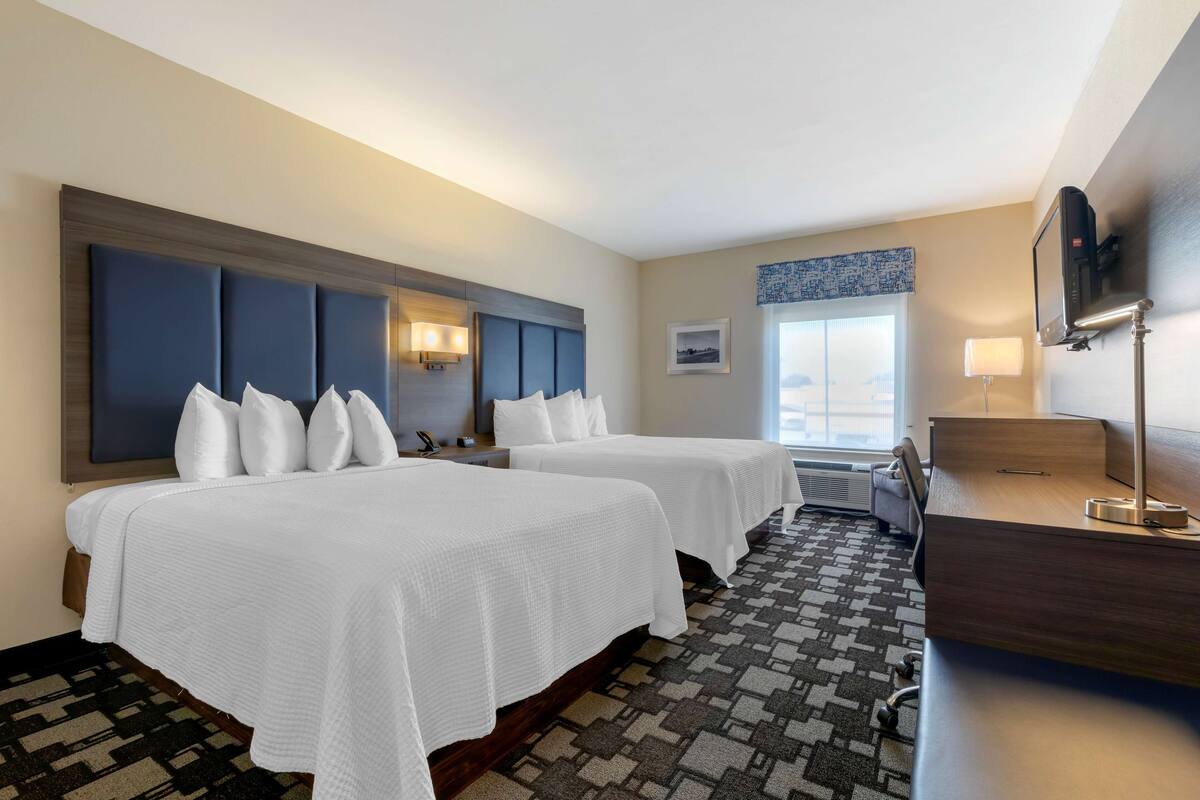 A hotel room with two beds, a desk, a chair, a TV, and a window with a view.