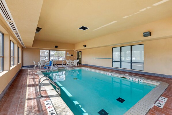 An indoor swimming pool with clear lane markings, a lifeguard chair, and a sunlit room with large windows.