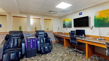 A massage therapy room with two massage chairs, a desk, a computer, and a TV.