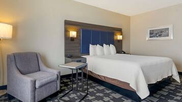 A hotel room with a bed, a chair, a small table, and two wall-mounted lamps.