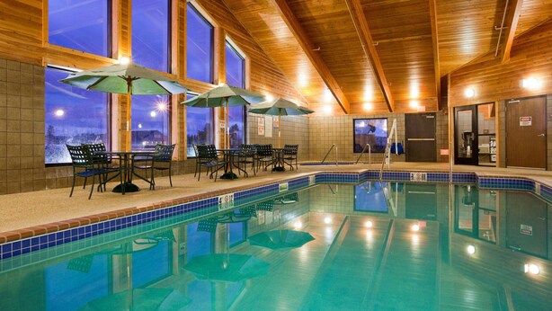 An indoor swimming pool with wooden ceiling beams, large windows, and several umbrellas. - AmericInn by Wyndham Thief River Falls (Thief River Falls)