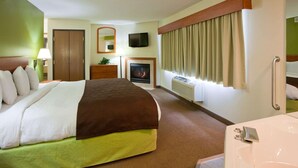 A hotel room with a bed, a television, a fireplace, a window with curtains, and a bathroom with a bathtub. - AmericInn by Wyndham Thief River Falls (Thief River Falls)