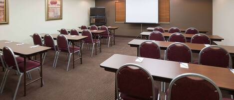 A conference room with tables and chairs, a projector screen, and a television.