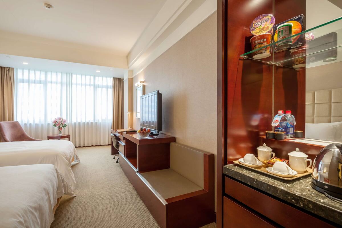 Une chambre d’hôtel avec deux lits, une télévision, un bureau avec un ordinateur, un coin café et un mini-bar.