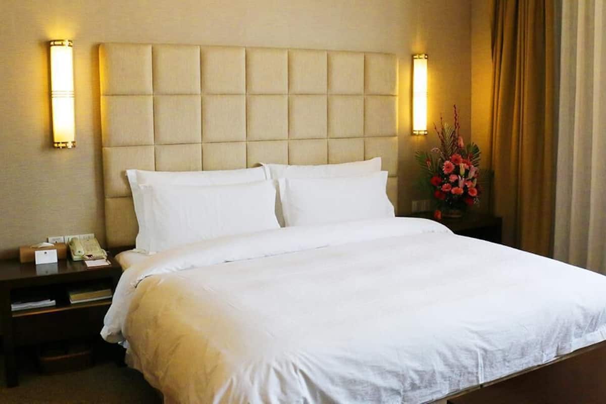 Une chambre d’hôtel avec un grand lit, une tête de lit à motifs rembourrés, deux lampes de chevet, une table de chevet avec un téléphone et un arrangement floral.