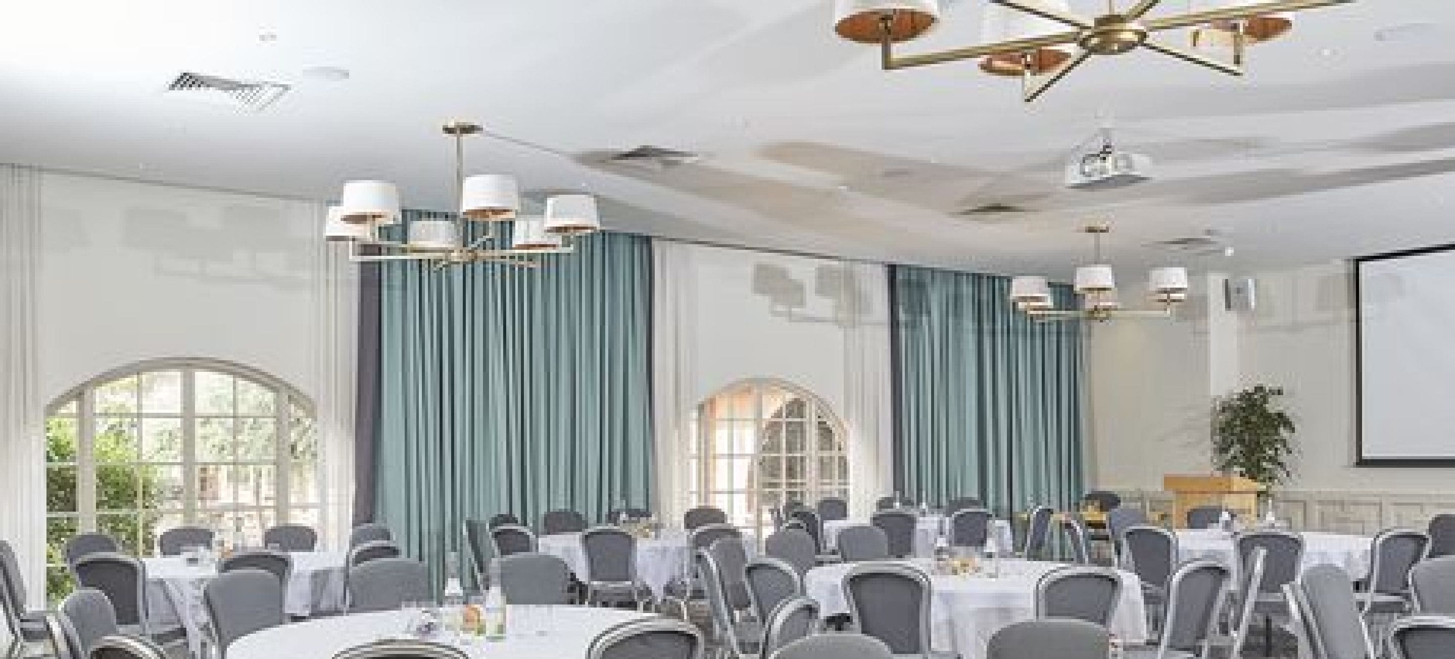Un salón de conferencias con mesas redondas, sillas y una pantalla para proyector.