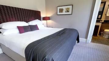 A hotel room with a large bed, a headboard with a patterned design, a bedside lamp, and a framed picture on the wall.