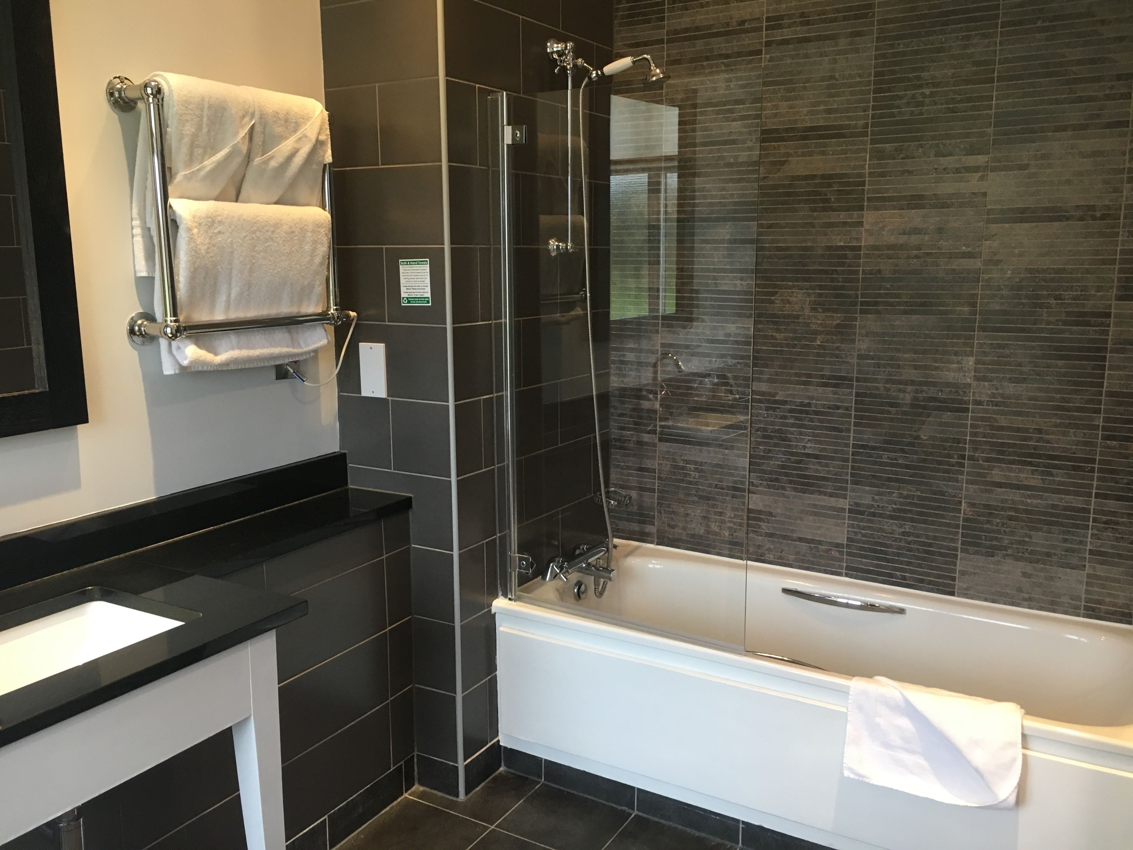 A modern bathroom with a glass-enclosed shower, a white bathtub, and a black countertop.