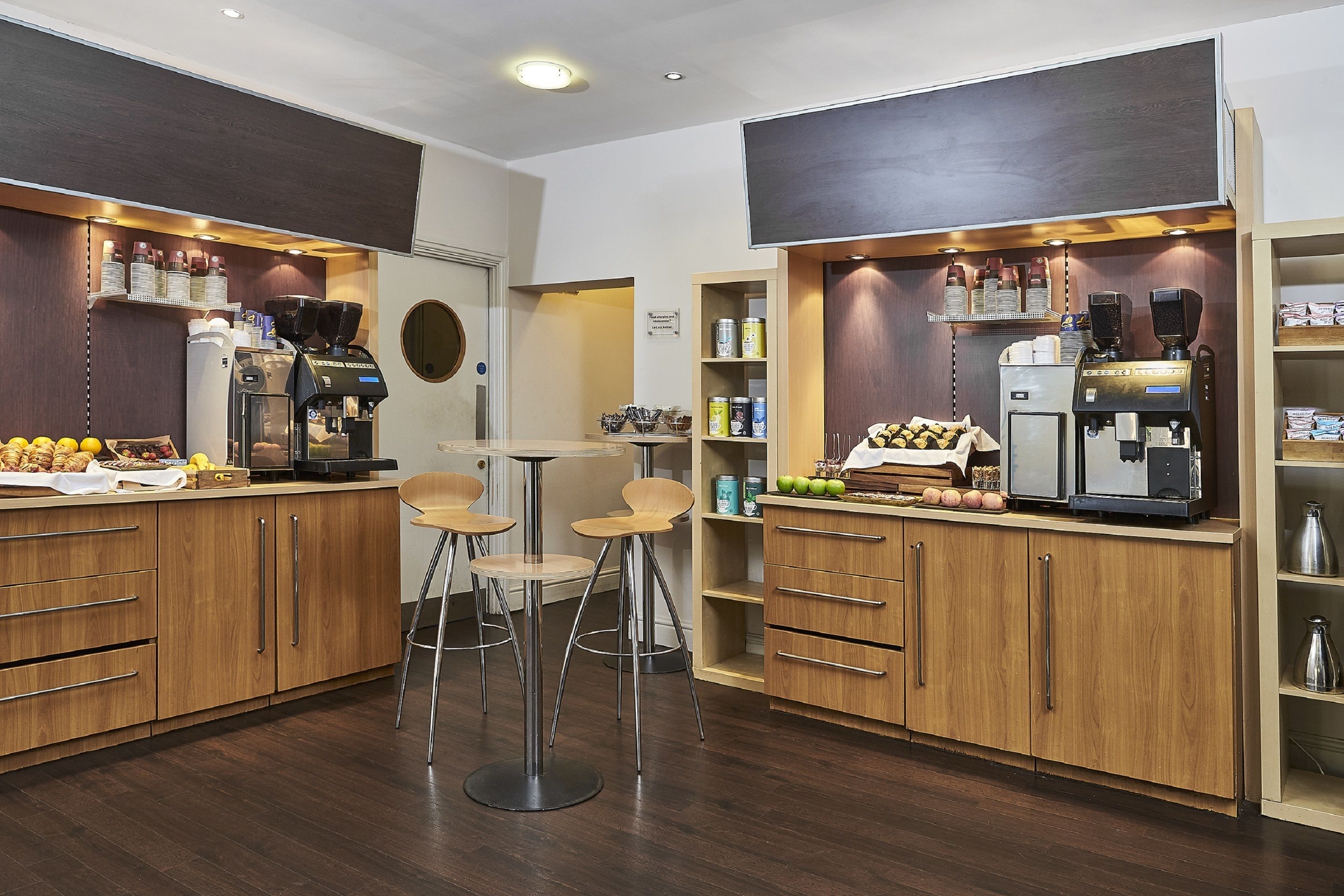 Een moderne koffiebar met twee espresso machines, houten kasten en barstoelen.