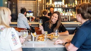 Un grupo de personas cenando en un restaurante con un bar al fondo.