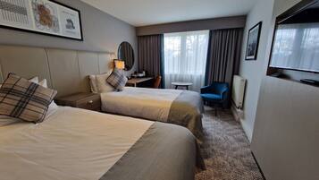A hotel room with two beds, a desk, a chair, a TV, and a window with curtains.