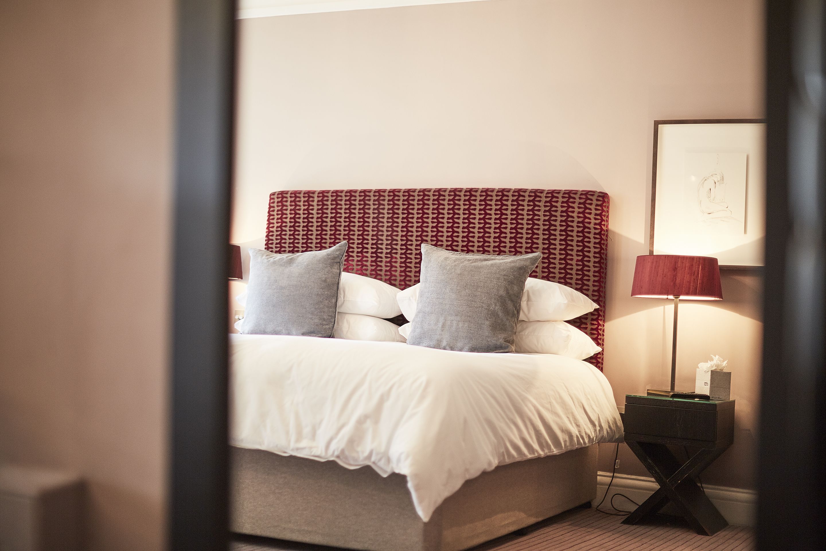 A neatly made bed with a patterned headboard, a bedside lamp, and a framed picture on the wall.