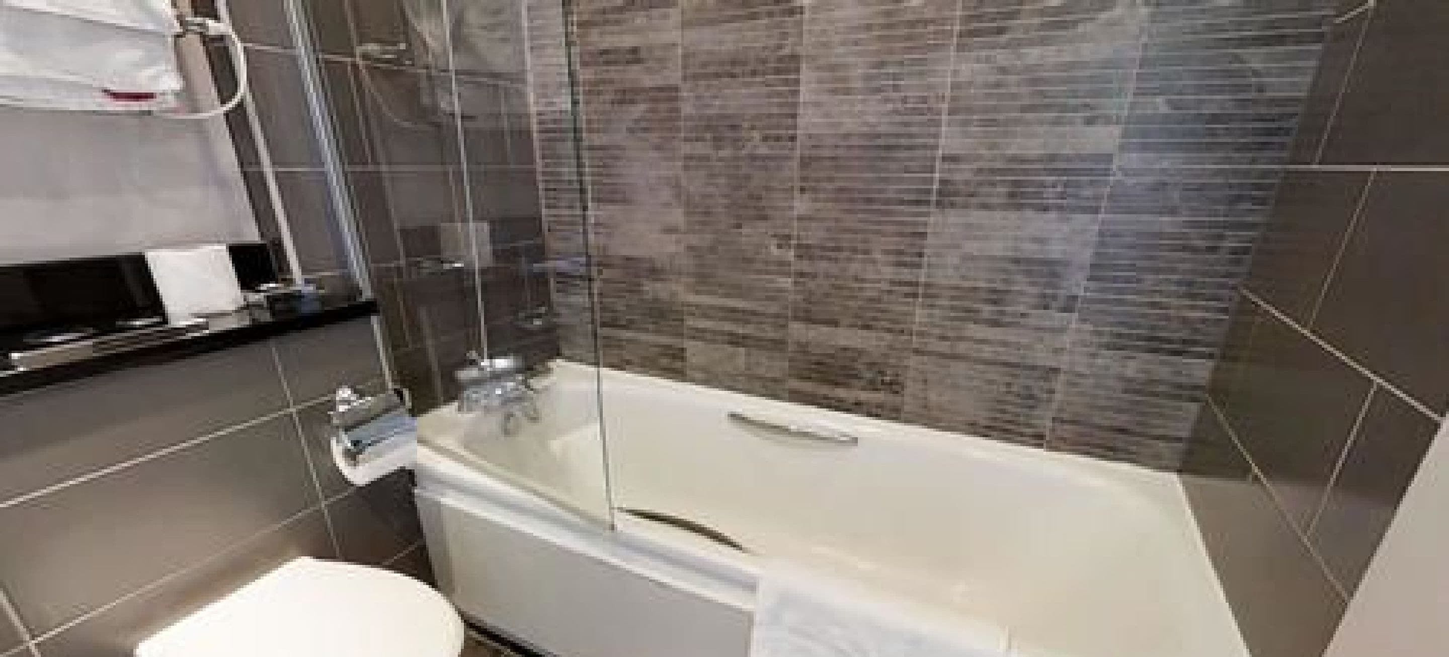 A modern bathroom with a glass-enclosed shower, a white bathtub, and a toilet.