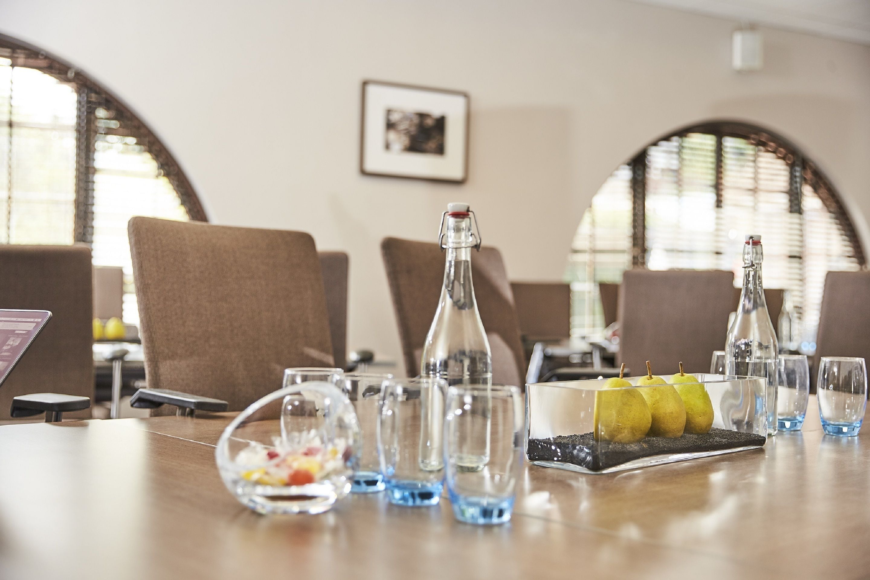 A dining table with chairs, clear glasses, a bottle, and a fruit bowl.
