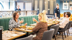Un restaurante con asientos tipo banqueta verdes, mesas de madera y lámparas colgantes.