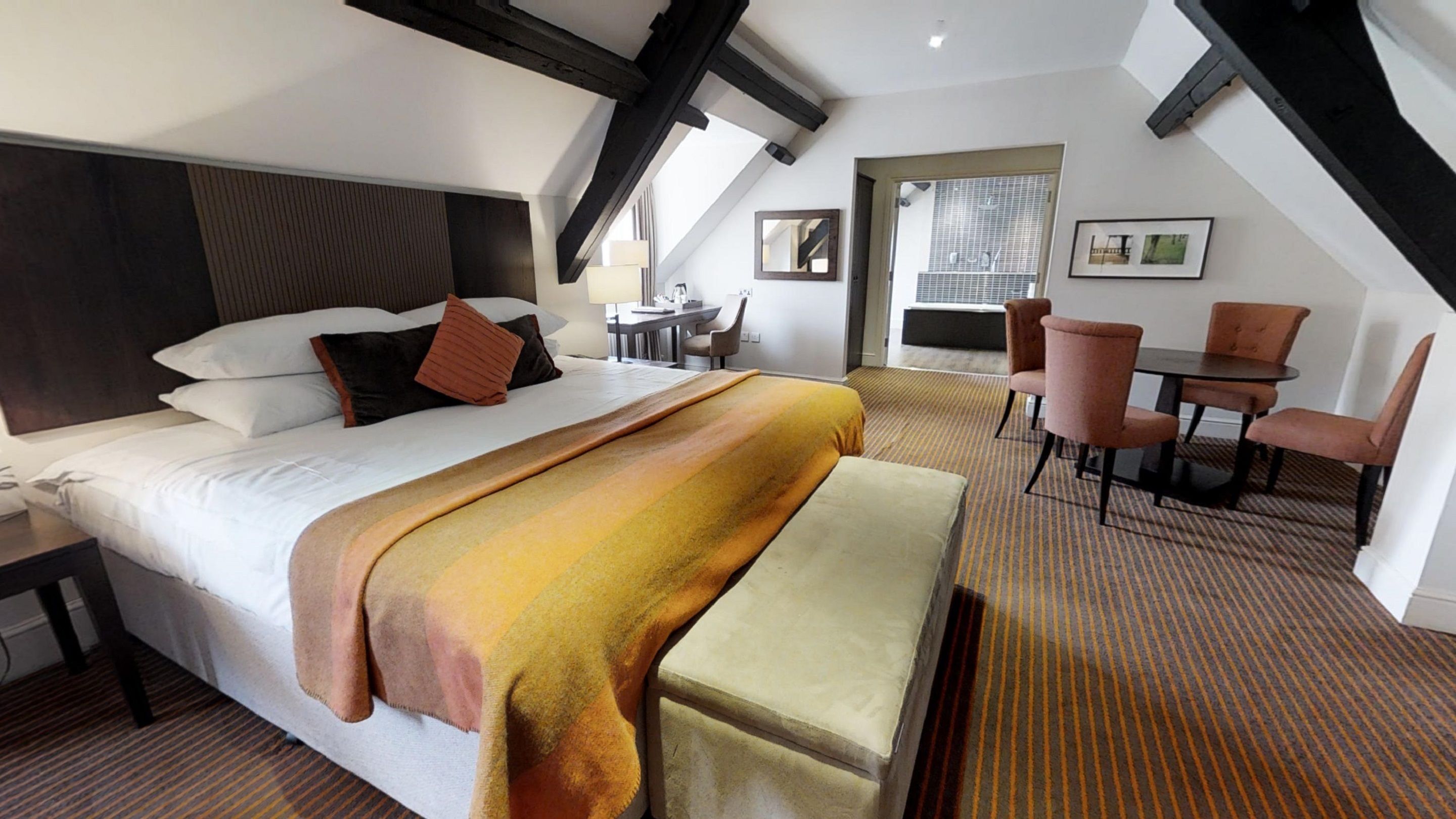 A modern hotel room with a large bed, a desk, and a dining area.
