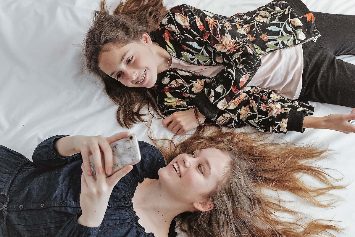 Two people lying on a bed with a white pillow and a black floral patterned shirt.