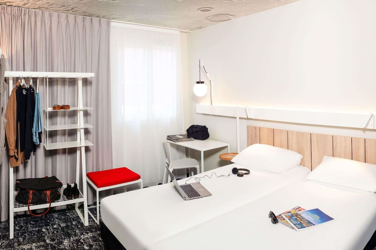 Ein Hotelzimmer mit Bett, Schreibtisch, Stuhl, Kleiderhaken und Kleiderschrank.
