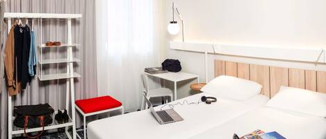 Una habitación de hotel con una cama, un escritorio, una silla, un perchero y un armario.