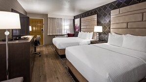 A hotel room with two beds, a desk with a chair, a TV, and a lamp.