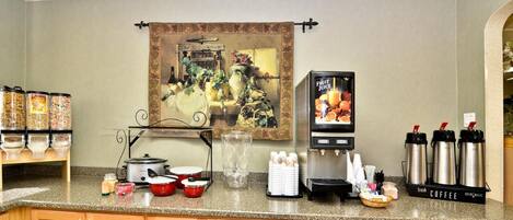 Un área de cocina con estación de café, dispensador de zumo de frutas y un cuadro en la pared.