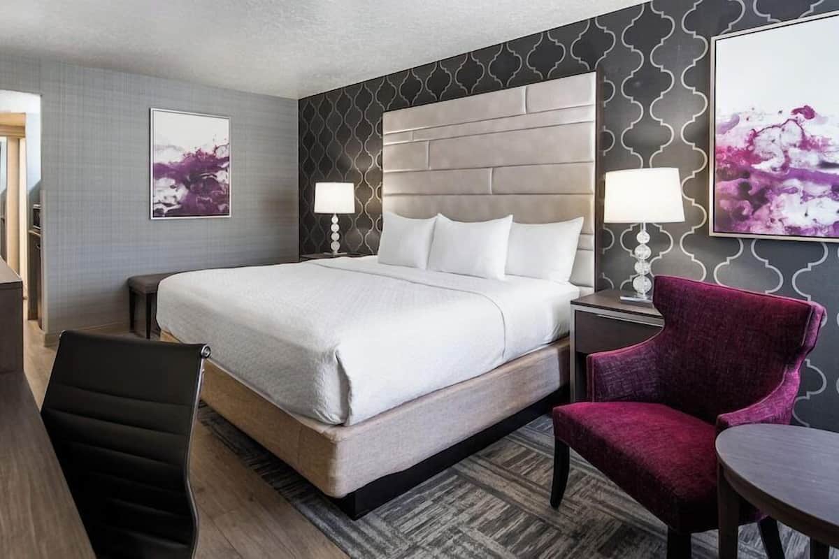 Una habitación de hotel con una cama grande, un escritorio, una silla y dos lámparas.