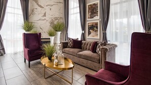 A modern living room with a sectional sofa, two armchairs, a round gold coffee table, and decorative plants.