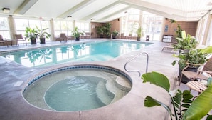 An indoor swimming pool with a hot tub, surrounded by chairs and potted plants.