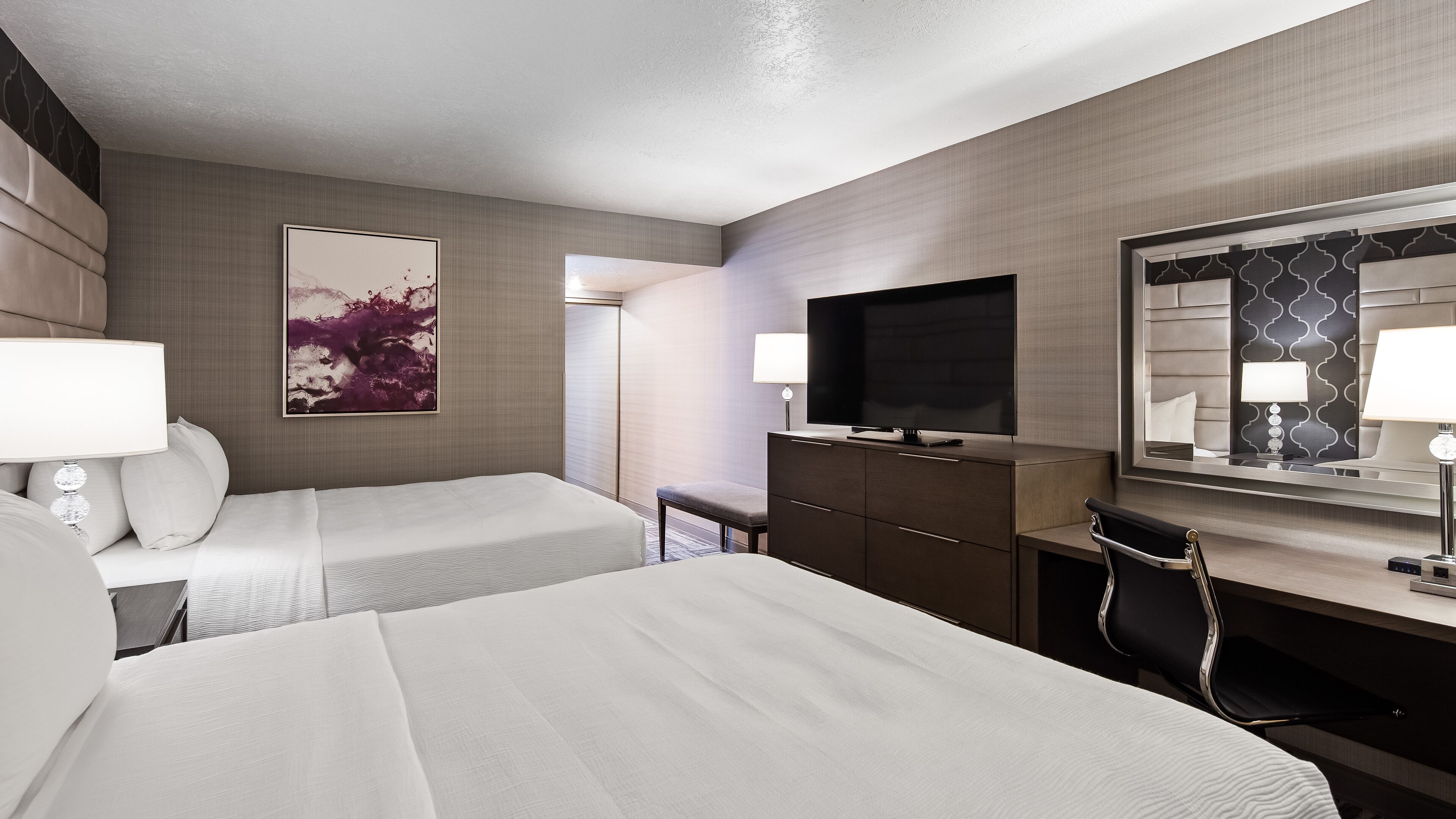 A hotel room with two beds, a flat-screen TV, a desk with a chair, and a large mirror.
