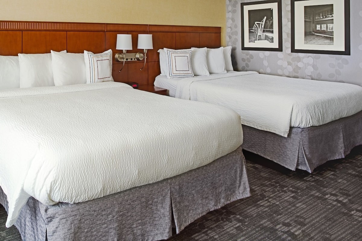 A hotel room with two beds, a chair, and a nightstand.
