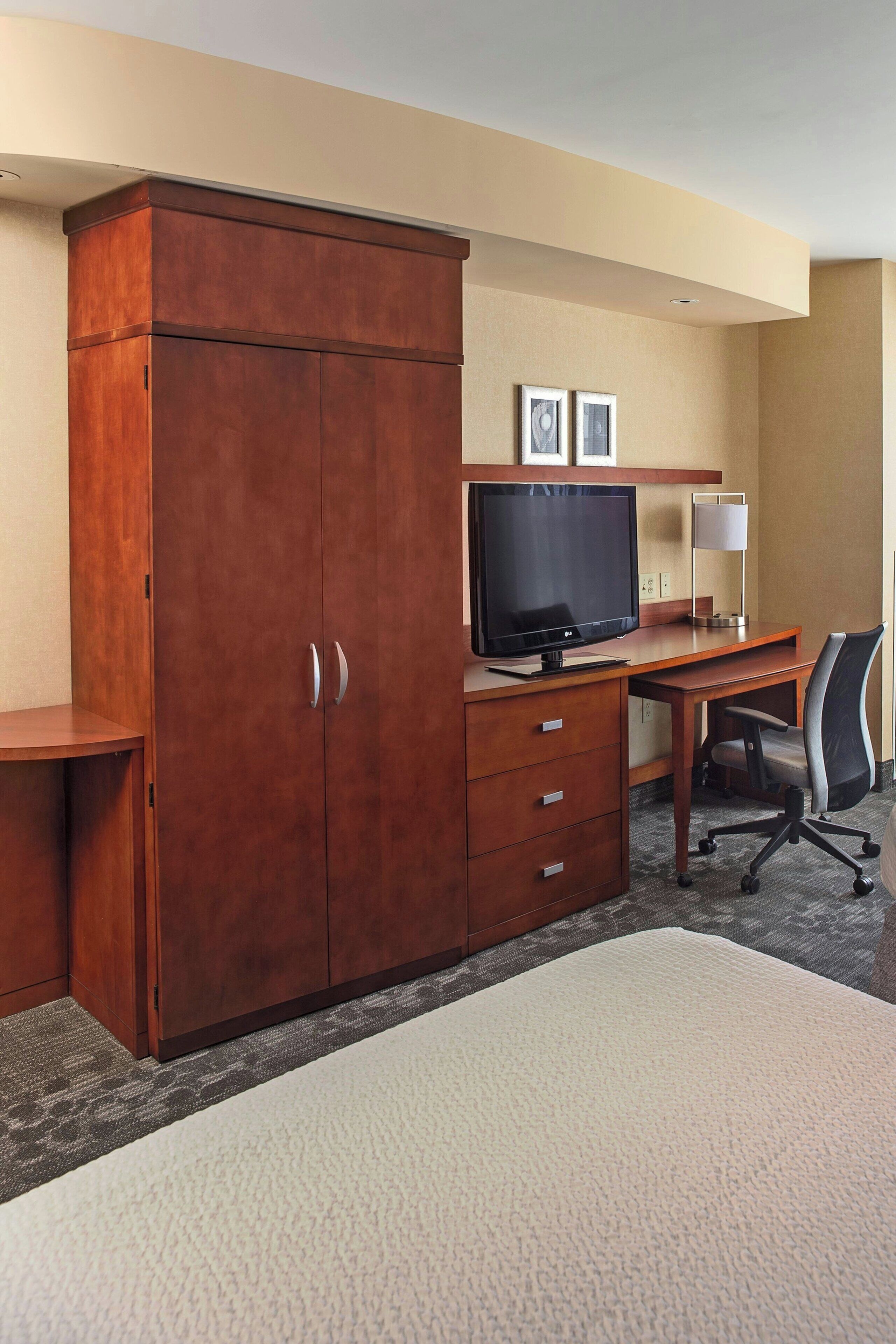 A hotel room with a wooden wardrobe, a desk with a computer, a television, and a lamp.