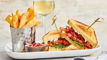 Een bord met een gegrilde sandwich, een glas witte wijn en een bak friet.