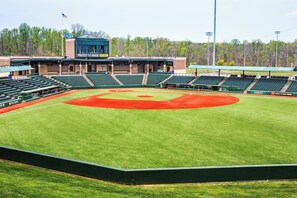 A baseball stadium with multiple seating sections, a central field marked with red dirt, and a scoreboard.
