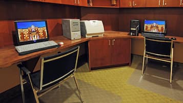 Ein Hotelzimmer mit Schreibtisch, zwei Stühlen, einem Computer, einem Drucker und einem Fernseher.