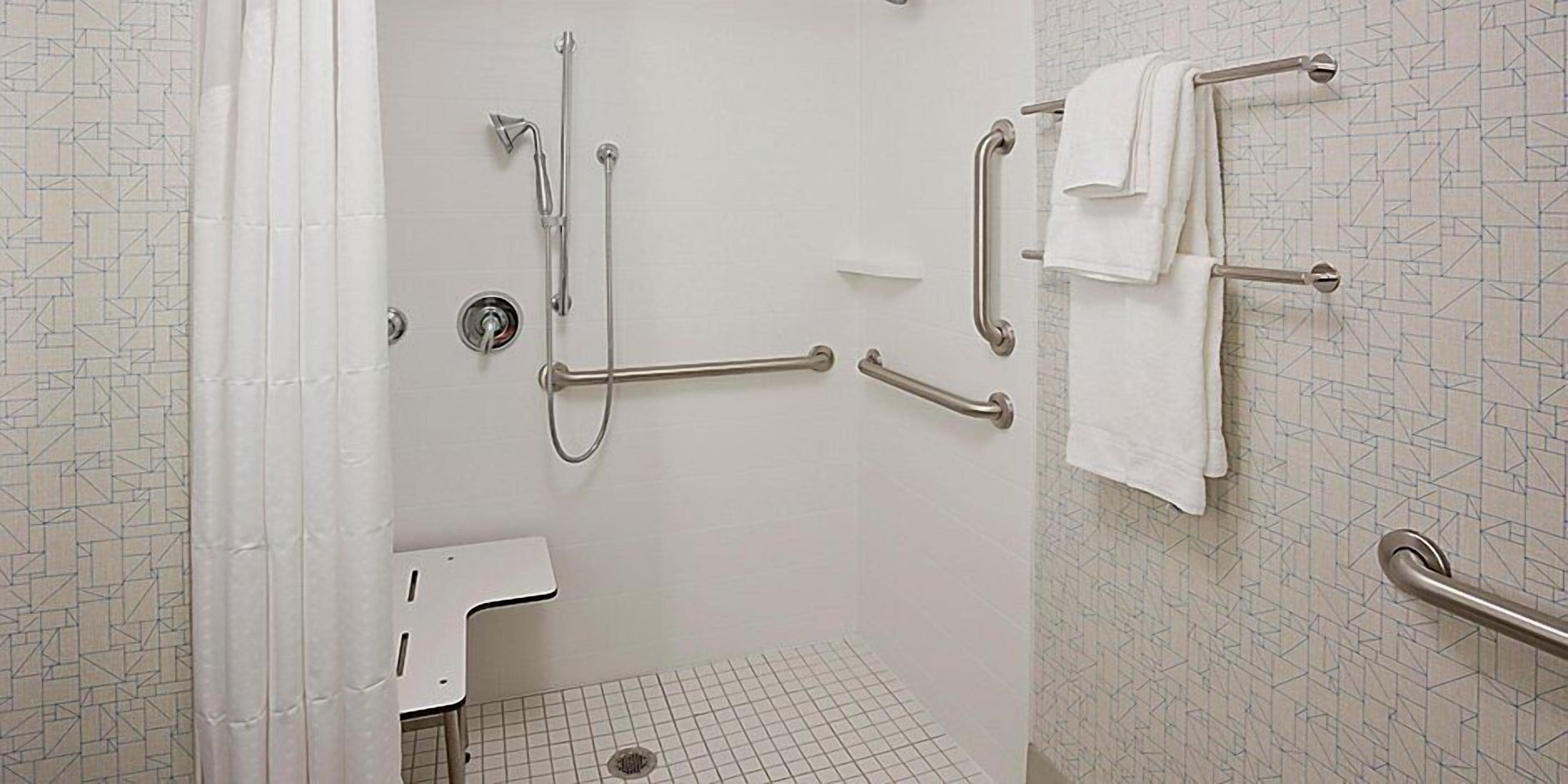A bathroom with a shower, grab bars, a toilet, and a towel rack.