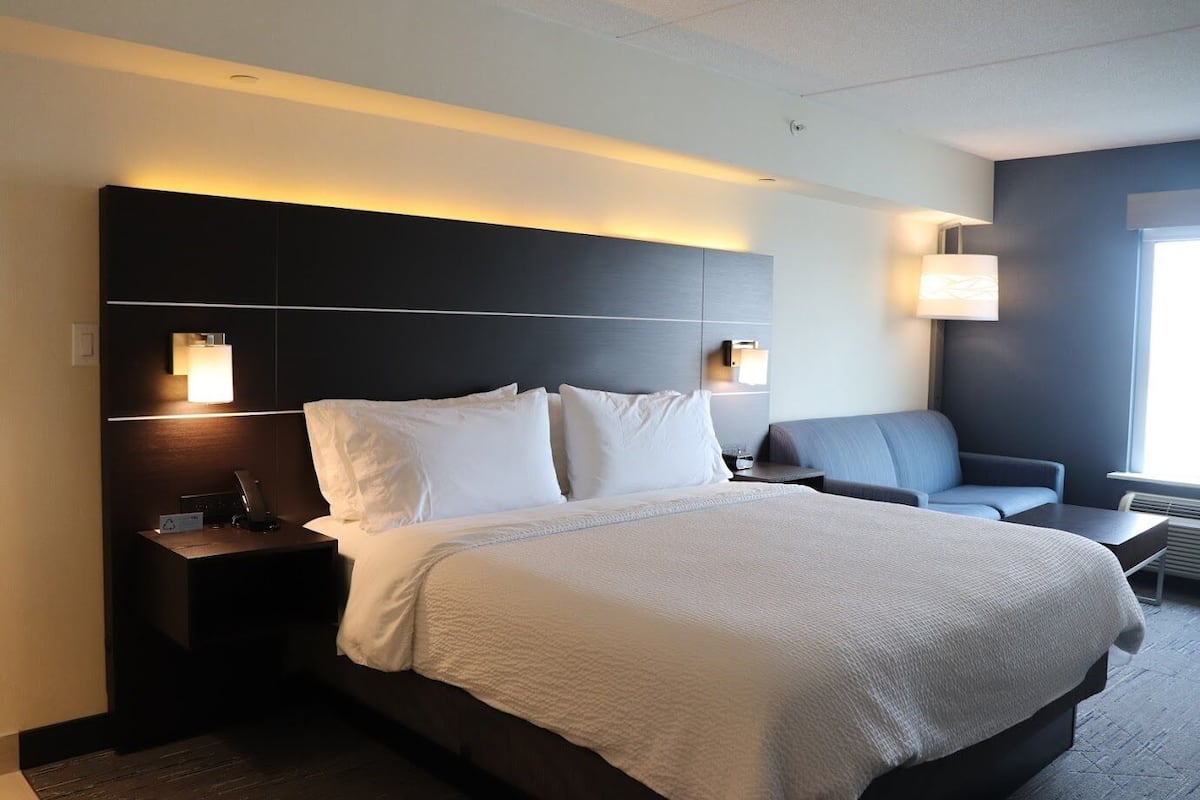 A modern hotel room with a large bed, a bedside table, a chair, and a nightstand.