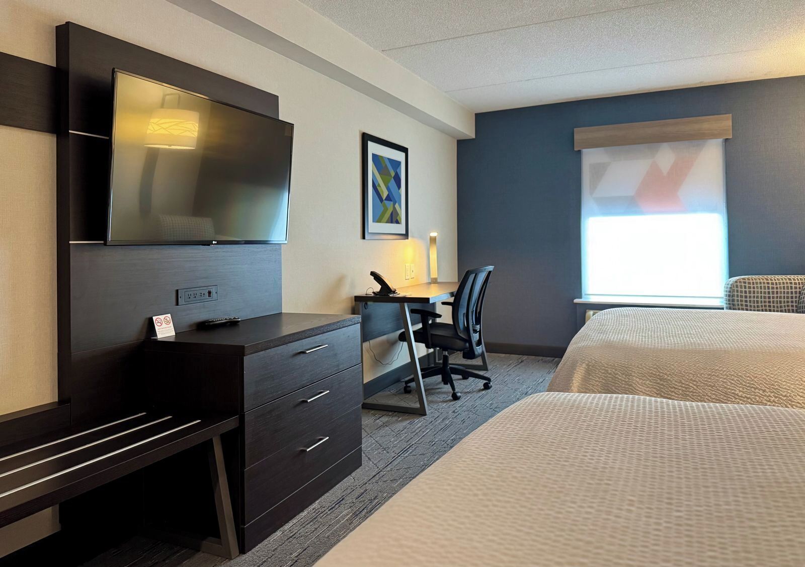 Habitación de hotel con cama, escritorio, silla, televisor y ventana.