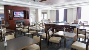 A hotel lobby with multiple dining tables and chairs, a television mounted on a wooden panel, and a reception desk. - Holiday Inn Express & Suites Brampton by IHG (Brampton)