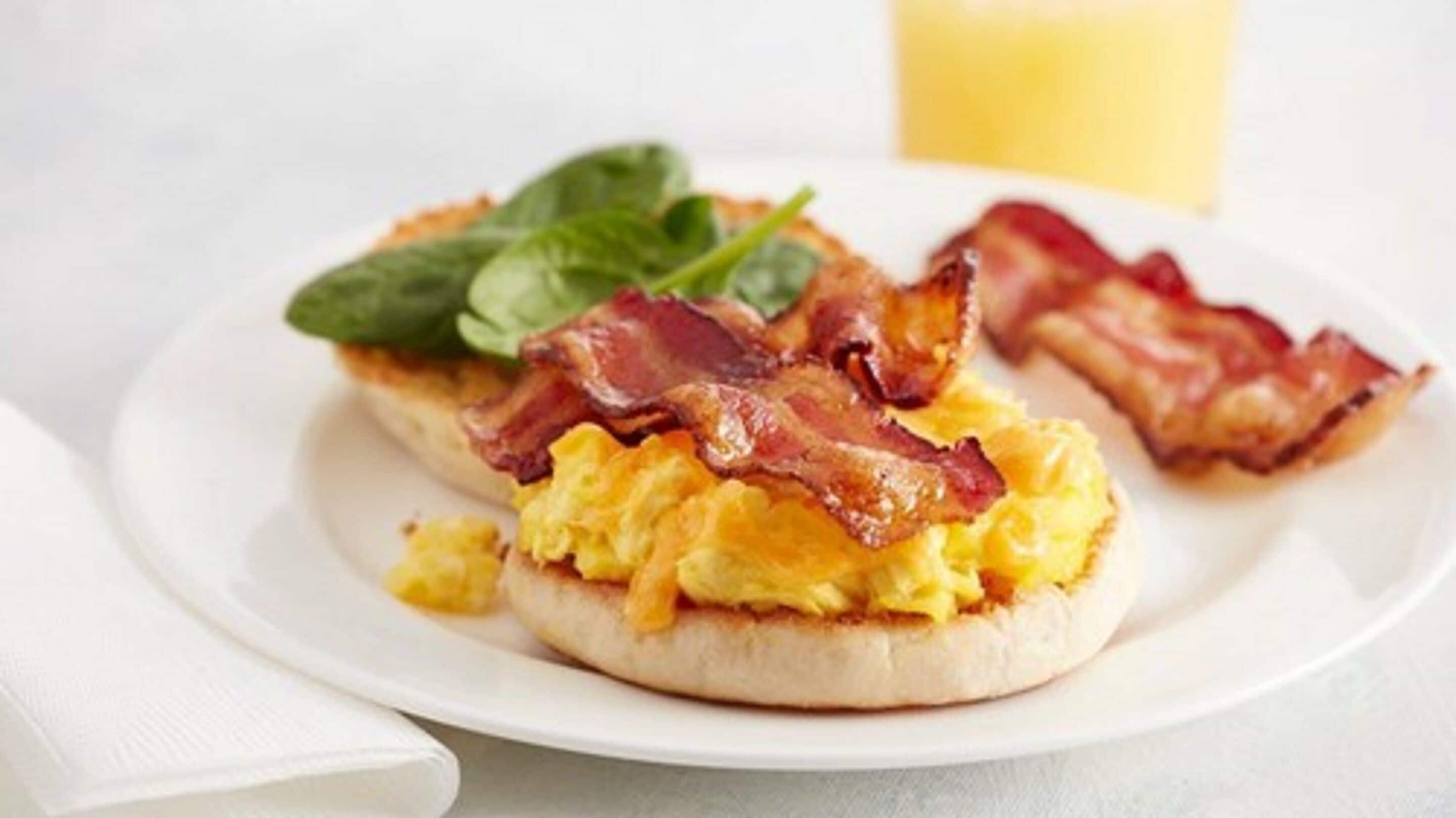 Un plato de desayuno con huevos revueltos, tocino y espinacas sobre un plato blanco.