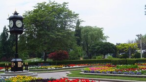 Ein Kirchturm in einem Park mit Blumenbeeten und Bäumen.