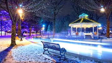 Un pabellón con el suelo cubierto de nieve y bancos, rodeado de árboles e iluminado por luces colgantes.