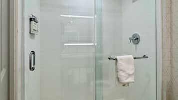 A glass-enclosed shower stall with a handheld showerhead, a towel rack, and a toilet visible in the adjacent room.