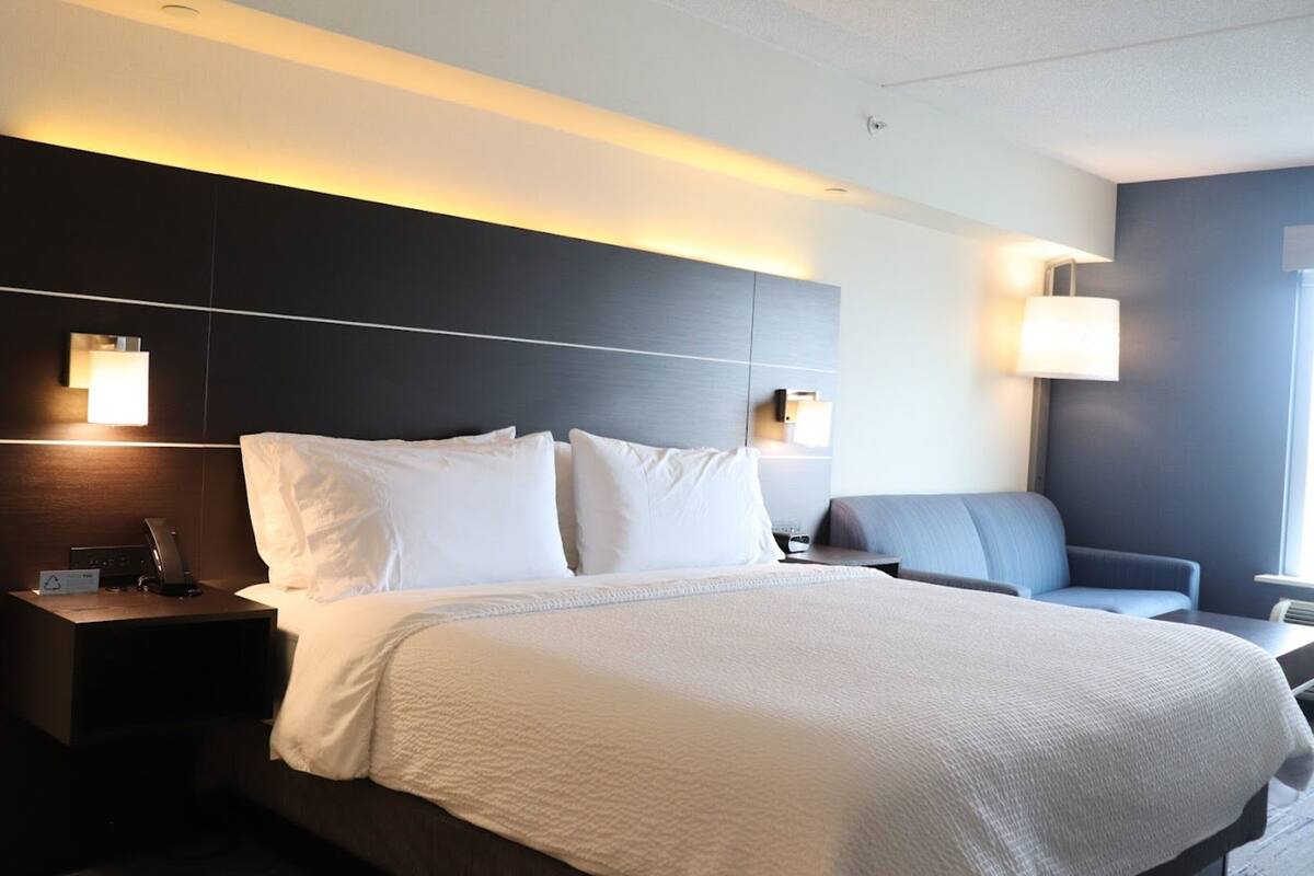 A modern hotel room with a large bed, bedside lamps, a desk, and a chair.