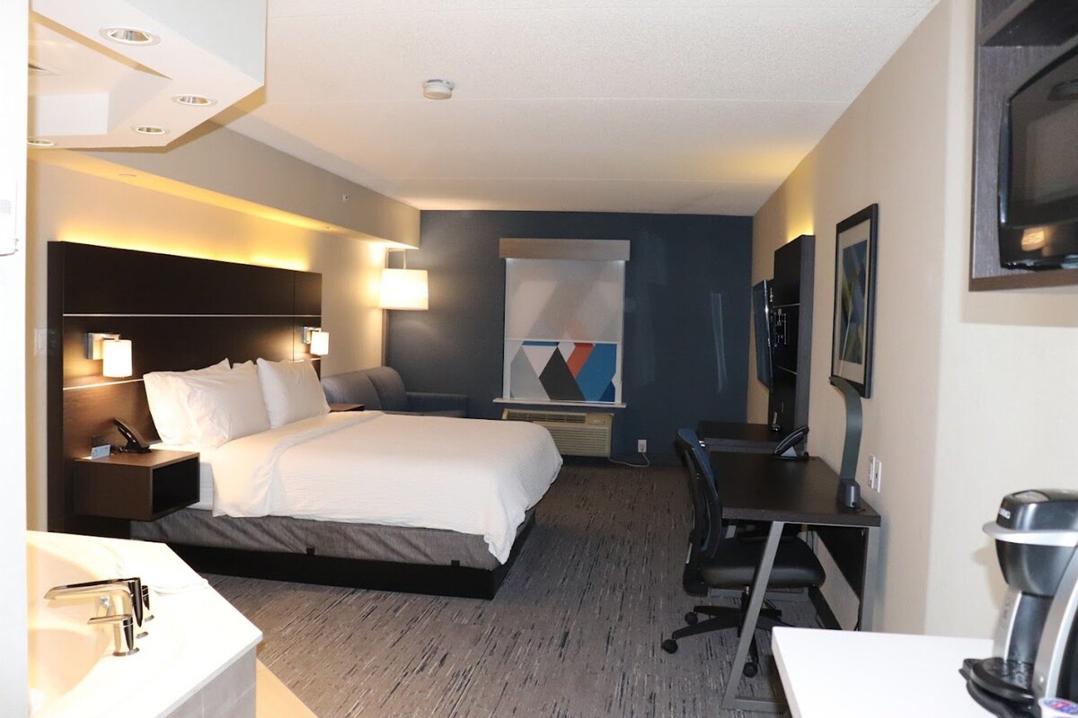 A hotel room with a bed, desk, chair, and a large window.