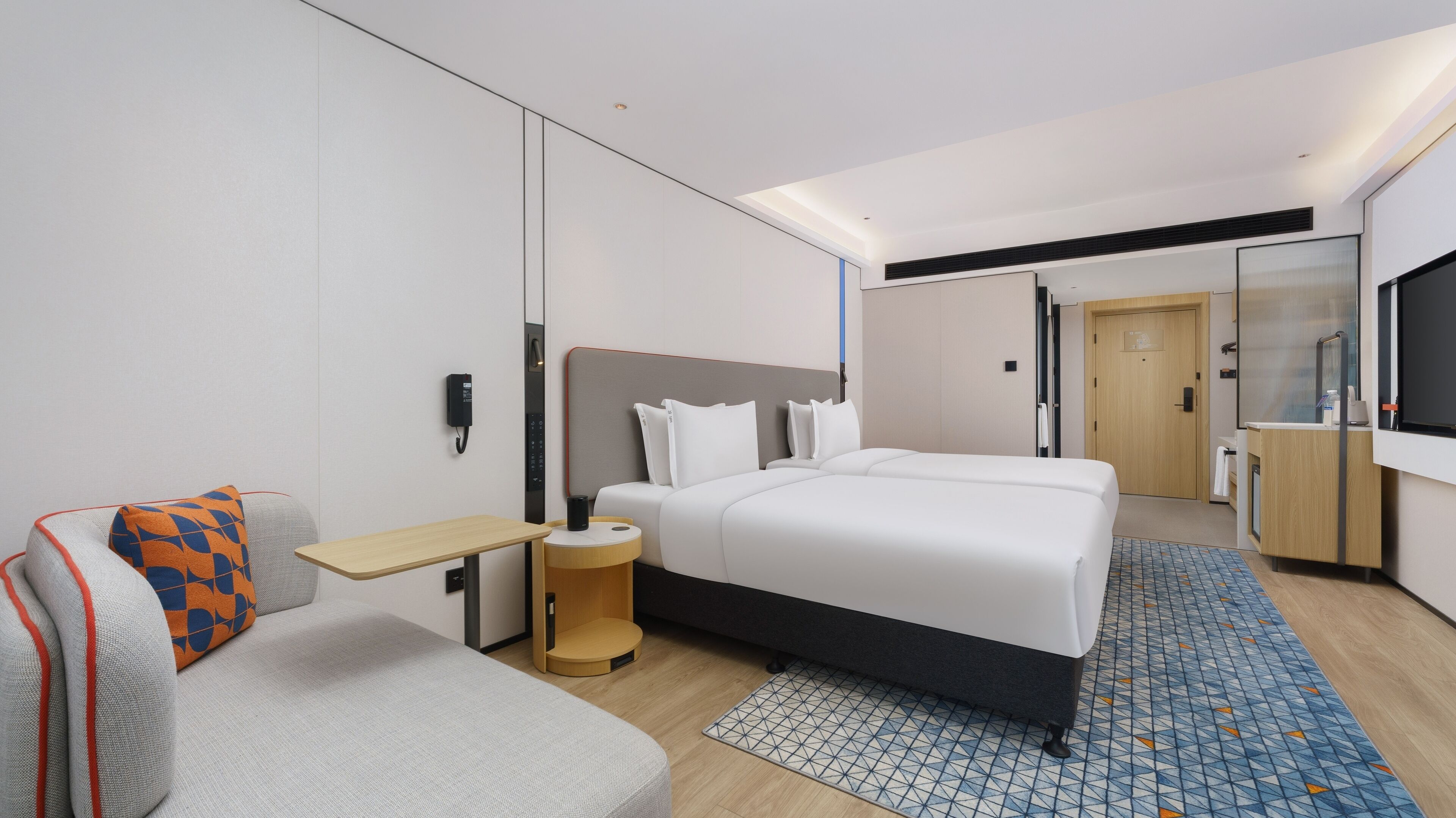 Une chambre d’hôtel moderne équipée d’un grand lit, d’un bureau, d’une chaise, d’une petite table et d’un téléviseur.
