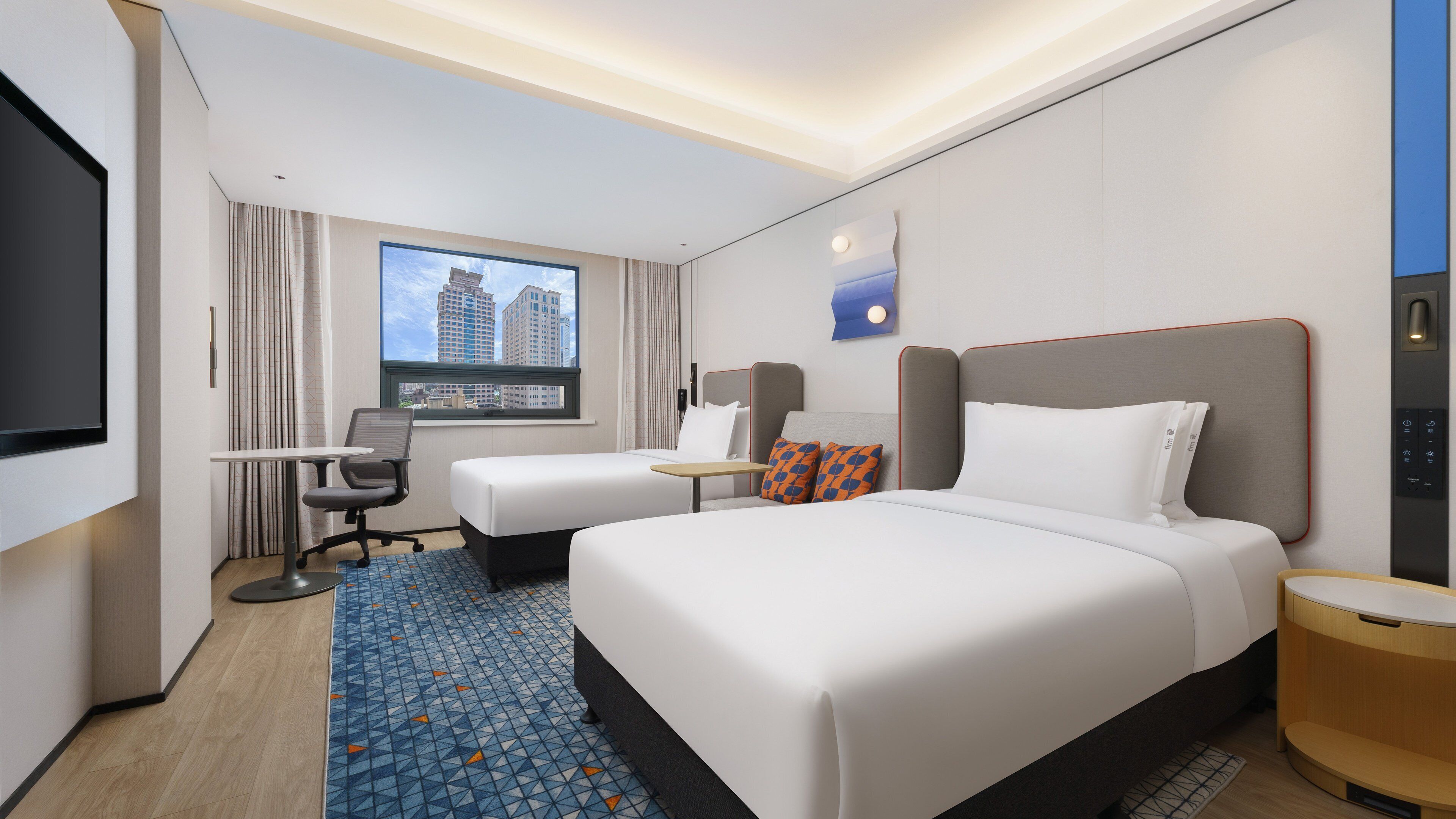 Habitación de hotel con cama, escritorio, silla, televisor y ventana con vista a la ciudad.