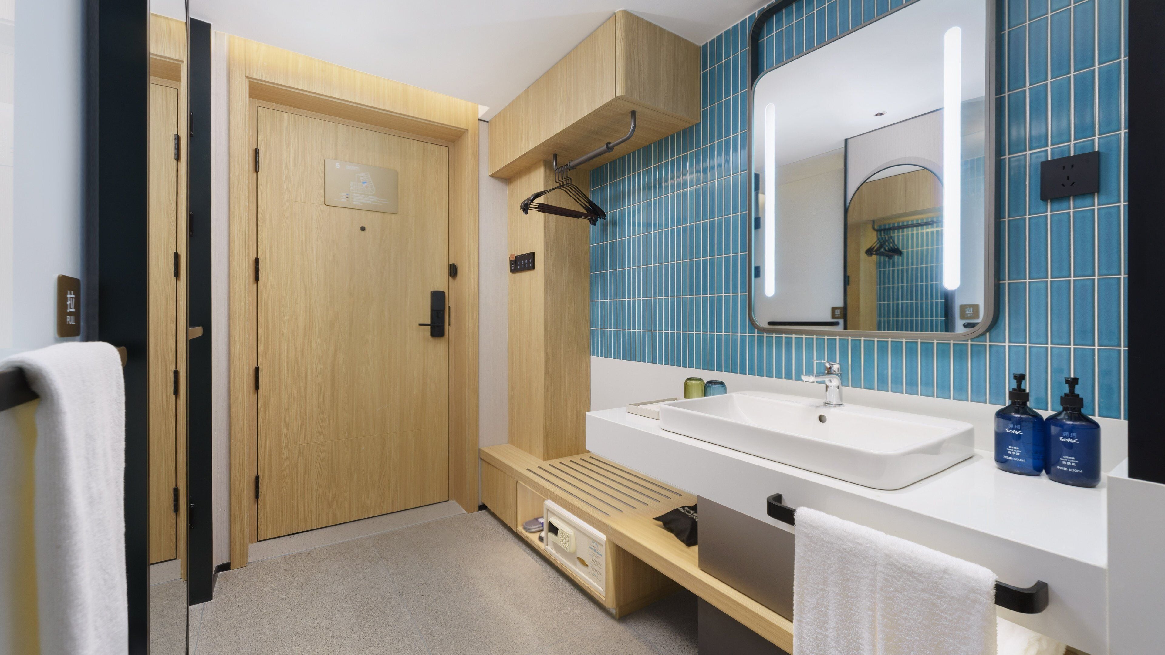 A modern bathroom with a wooden door, a sink with a mirror, and blue-tiled walls.